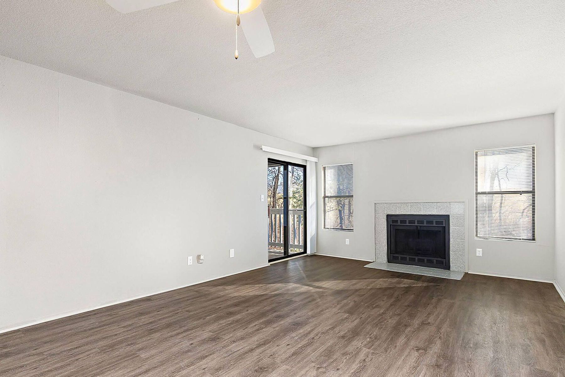 Empty room with wood floors, ceiling fan, and sliding glass door leading to a patio with vertical blinds at Apex West Midown.